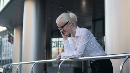 Beautiful young business woman calling by phone on the background of skyscrapersの写真素材