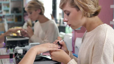 Closeup shot of a woman in a nail salon receiving a manicure by a beautician with nail file. Woman getting nail manicure. Beautician file nails to a customer. Blurred backgroundの写真素材
