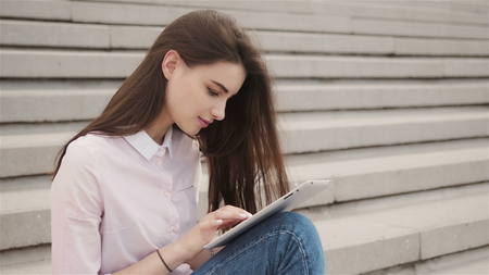 Young student using a tablet computer outside a building
