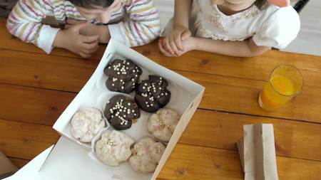 little daughter girl and boy child opening box with desserts sweets on kitchen, top viewの写真素材