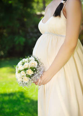 the pregnant woman in a cream dress with a bunch of flowersの写真素材