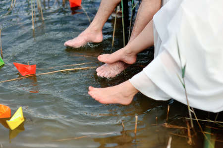 Bare feet of the newly-married couple hang down over water where paper ships floatの写真素材
