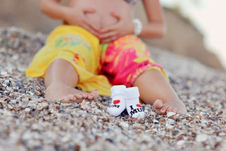 on sand the pregnant woman and a close up of her foot and children s socks sitsの写真素材