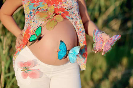 stomach of the pregnant woman and multi-colored butterfliesの写真素材
