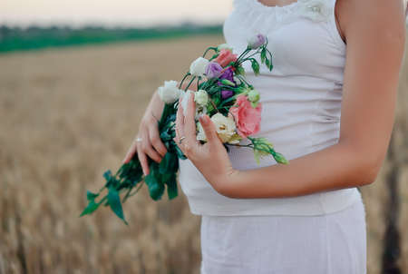 Silhouette of the pregnant woman with a bouquet of wild flowers