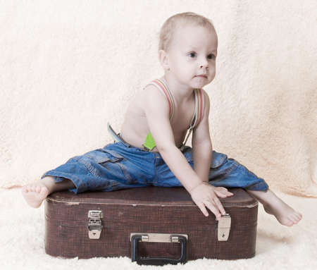 the child in jeans sits on an old suitcaseの写真素材