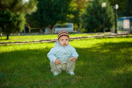 against green bushes the kid in a sweater and a cap