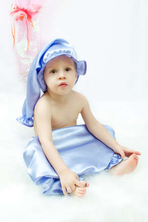 on a white background and a pink curtain the child in a sleeping suit and a cap sitsの写真素材