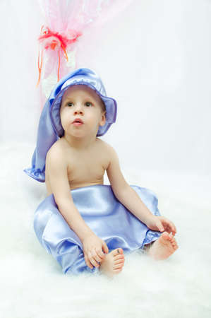 on a white background and a pink curtain the child in a sleeping suit and a cap sitsの写真素材