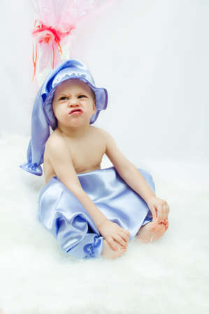 on a white background and a pink curtain the child in a sleeping suit and a cap sitsの写真素材