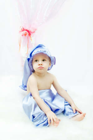 on a white background and a pink curtain the child in a sleeping suit and a cap sitsの写真素材