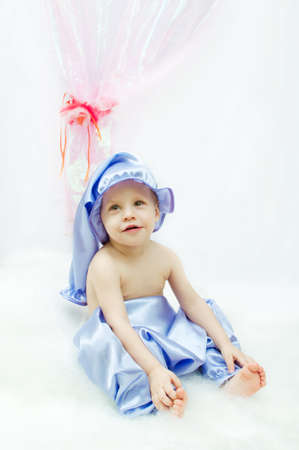 on a white background and a pink curtain the child in a sleeping suit and a cap sitsの写真素材