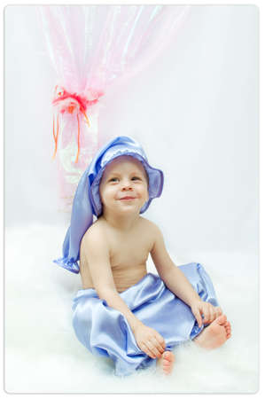 on a white background and a pink curtain the child in a sleeping suit and a cap sitsの写真素材