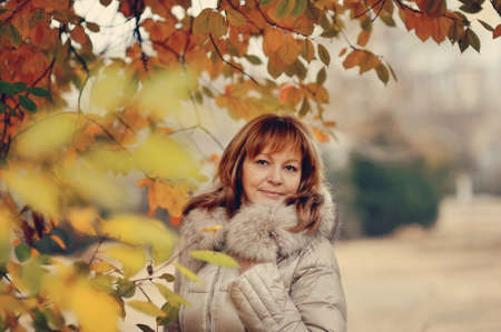 the woman in a white coat poses in the autumn woodの写真素材