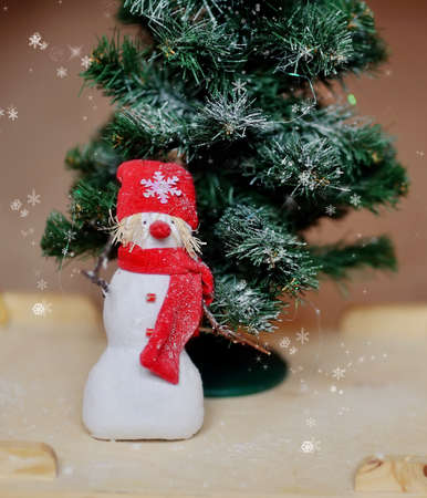 toy angel a snowman in a red cap under a fir-treeの写真素材
