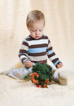 on a light background the boy in a striped sweater sits and decorates a fir-treeの写真素材