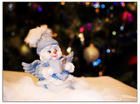 toy angel a snowman in a blue cap under a fir-treeの写真素材