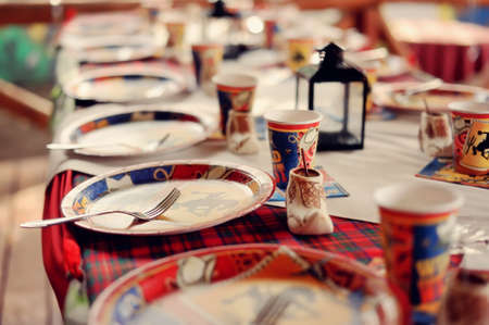 the long banquet table is decorated with color plates and cups for childrenの写真素材
