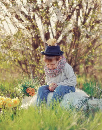 boy sitting outdoors in a hat with ducks and chickensの写真素材