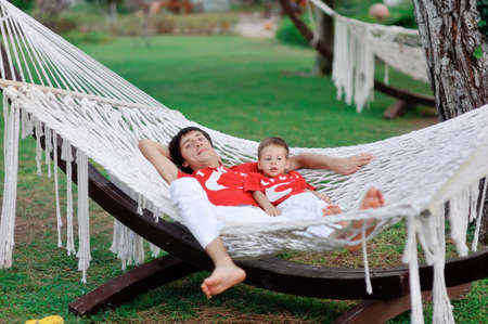 outdoors in a white hammock resting father and son in red shirtsの写真素材