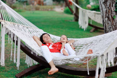 outdoors in a white hammock resting father and son in red shirtsの写真素材