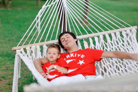 outdoors in a white hammock resting father and son in red shirtsの写真素材