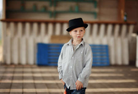 beautiful child in a black hat and jeans posing on a wooden floorの写真素材