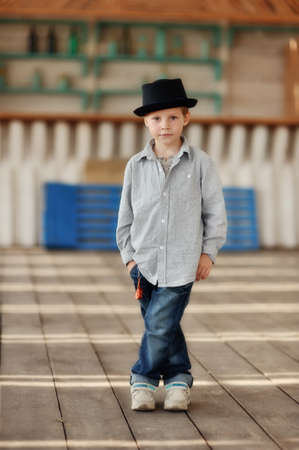 beautiful child in a black hat and jeans posing on a wooden floorの写真素材