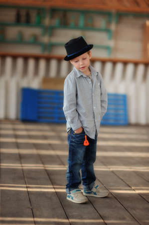 beautiful child in a black hat and jeans posing on a wooden floorの写真素材