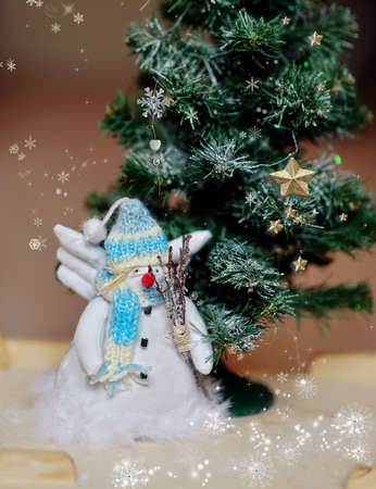 toy angel a snowman in a blue cap under a fir-treeの写真素材