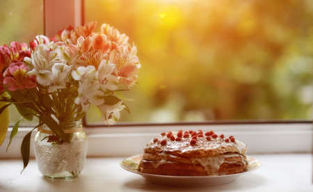 against the background of the window is a cake with berries and a bouquet of flowers near