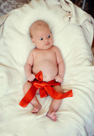 naked baby lying on a blanket with a red ribbonの写真素材