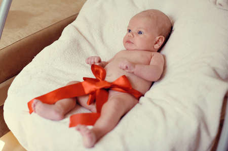 naked baby lying on a blanket with a red ribbonの写真素材