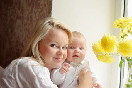 feminine mother tenderly embracing her child at the window with flowersの写真素材