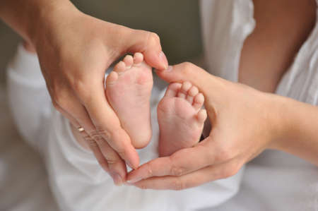 Mother s hands holding a heart-shaped feet of a newborn babyの写真素材