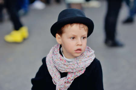 stylish, thoughtful boy in a black coat and hat with a beautiful scarf