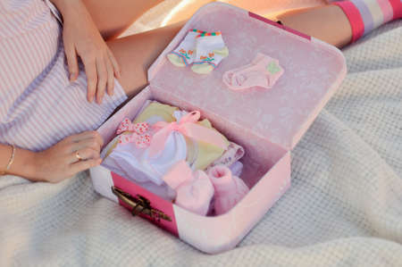 Pretty pregnant woman with childrens clothes at homeの写真素材