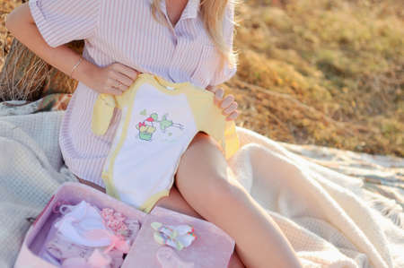 Pretty pregnant woman with childrens clothes at homeの写真素材
