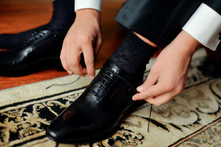 hands of the groom tied the laces on black shoesの写真素材