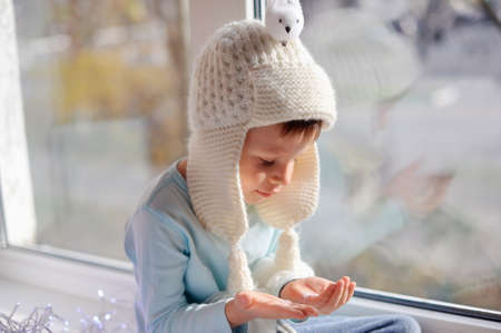 winter boy sitting by the window in a white knitted cap