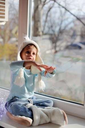 winter boy sitting by the window in a white knitted capの写真素材