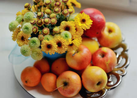 on a white background ripe apples, mandarin bright bouquet of autumn flowers in the windowの写真素材