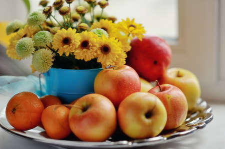 on a white background ripe apples, mandarin bright bouquet of autumn flowers in the windowの写真素材