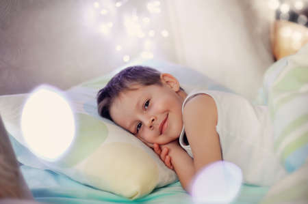 the little boy woke up in a children s cozy bed of lightsの写真素材