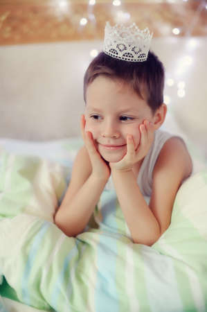 the boy woke up and is sitting in bed with a crown on his headの写真素材