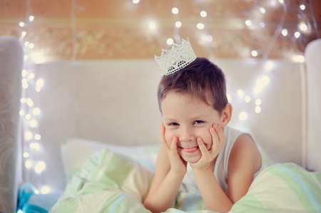 the boy woke up and is sitting in bed with a crown on his headの写真素材