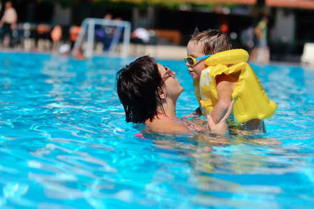 In the sunny day in the summer the boy in sun glasses and in a life jacket plays pool with mumの写真素材