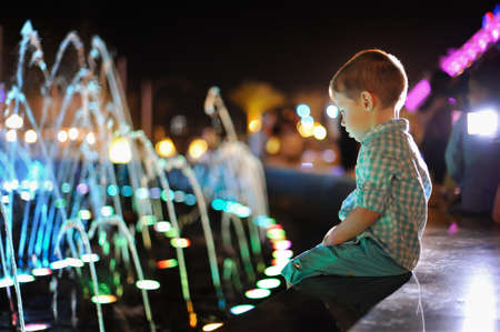in the evening the boy was sitting by the fountain in multicolored lightsの写真素材