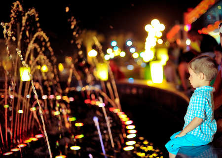 in the evening the boy was sitting by the fountain in multicolored lightsの写真素材