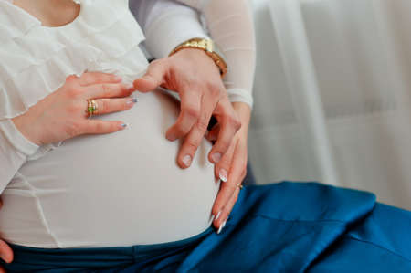 close-up of pregnant woman s belly in white hands hugging her husbandの写真素材